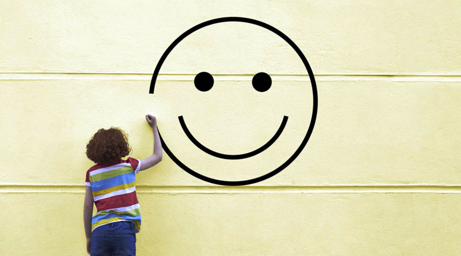 Image of a child drawing a big happy face on a wall.